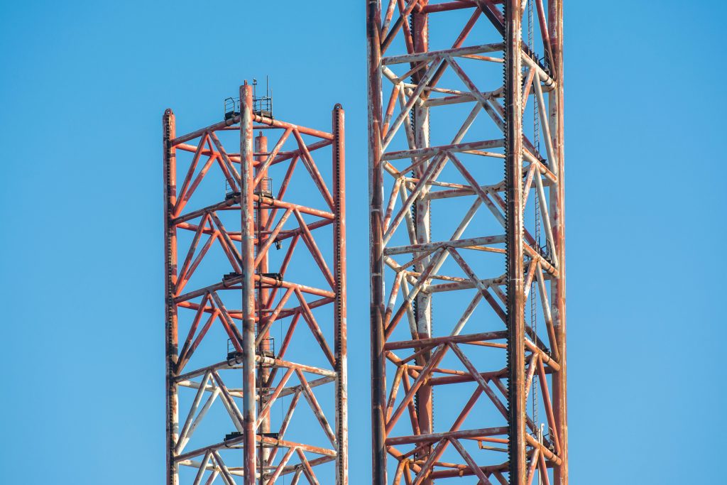Close-up view of rusty crane towers under clear blue sky, illustrating construction industry details.