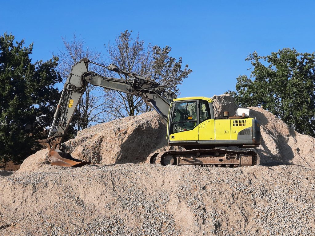 A yellow excavator working on a gravel mound at a construction site.
