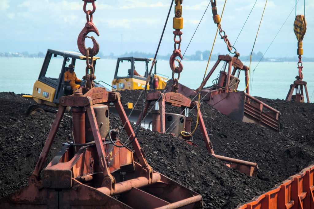 Heavy machinery loading coal at a port with a clear sky reflecting on the water.